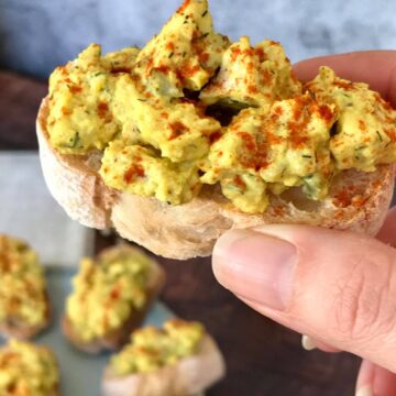 Hand holding a piece of vegan deviled egg crostini.