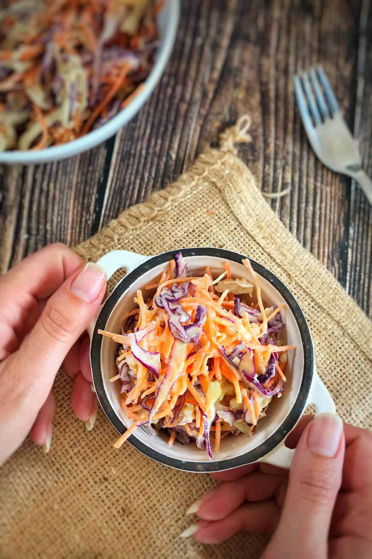Hand holding a small bowl of vegan coleslaw.