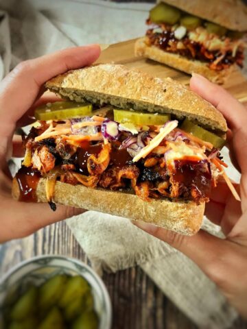 Hands holding a vegan BBQ jackfruit sandwich.