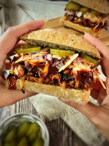 Hands holding a vegan BBQ jackfruit sandwich.