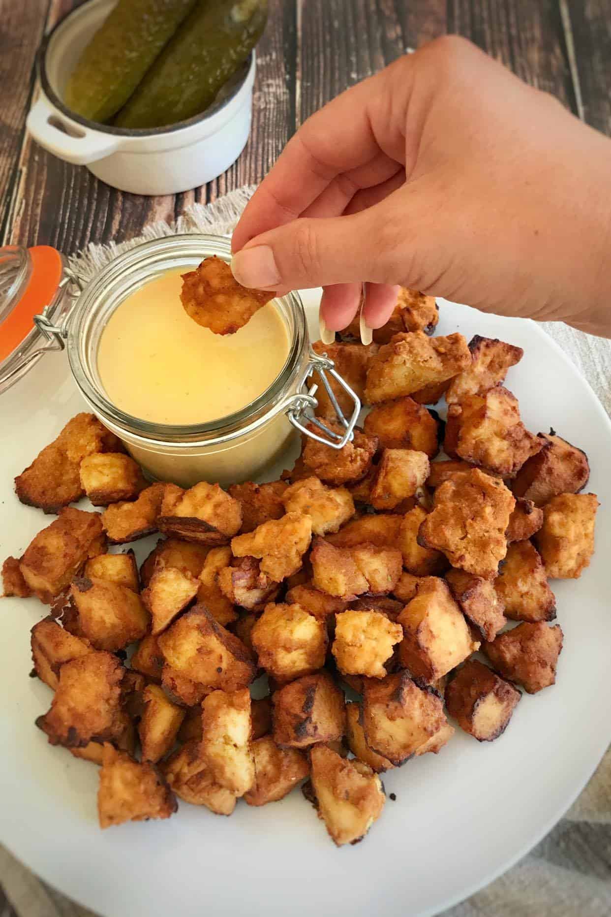 Hand dipping tofu nugget into vegan honey mustard dressing.