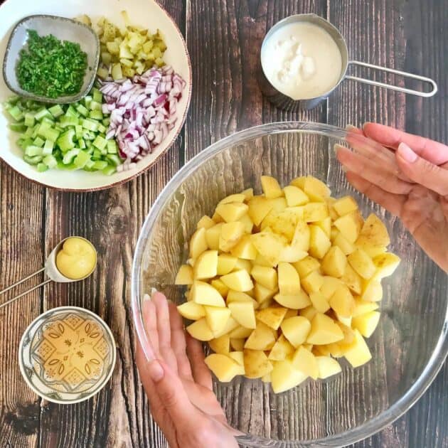 Cooked potatoes in a bowl with other potato salad ingredients.