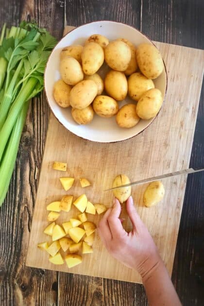 Hand cubing potatoes on a cutting board.