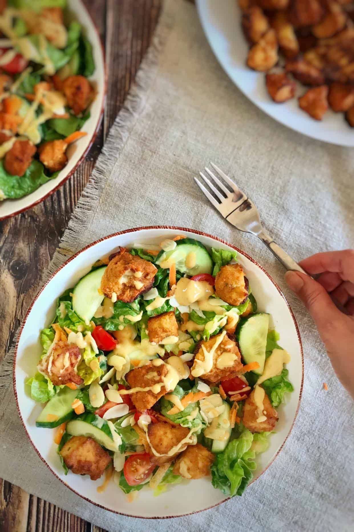 Hand picking up a fork next to a bowl of crispy tofu salad.