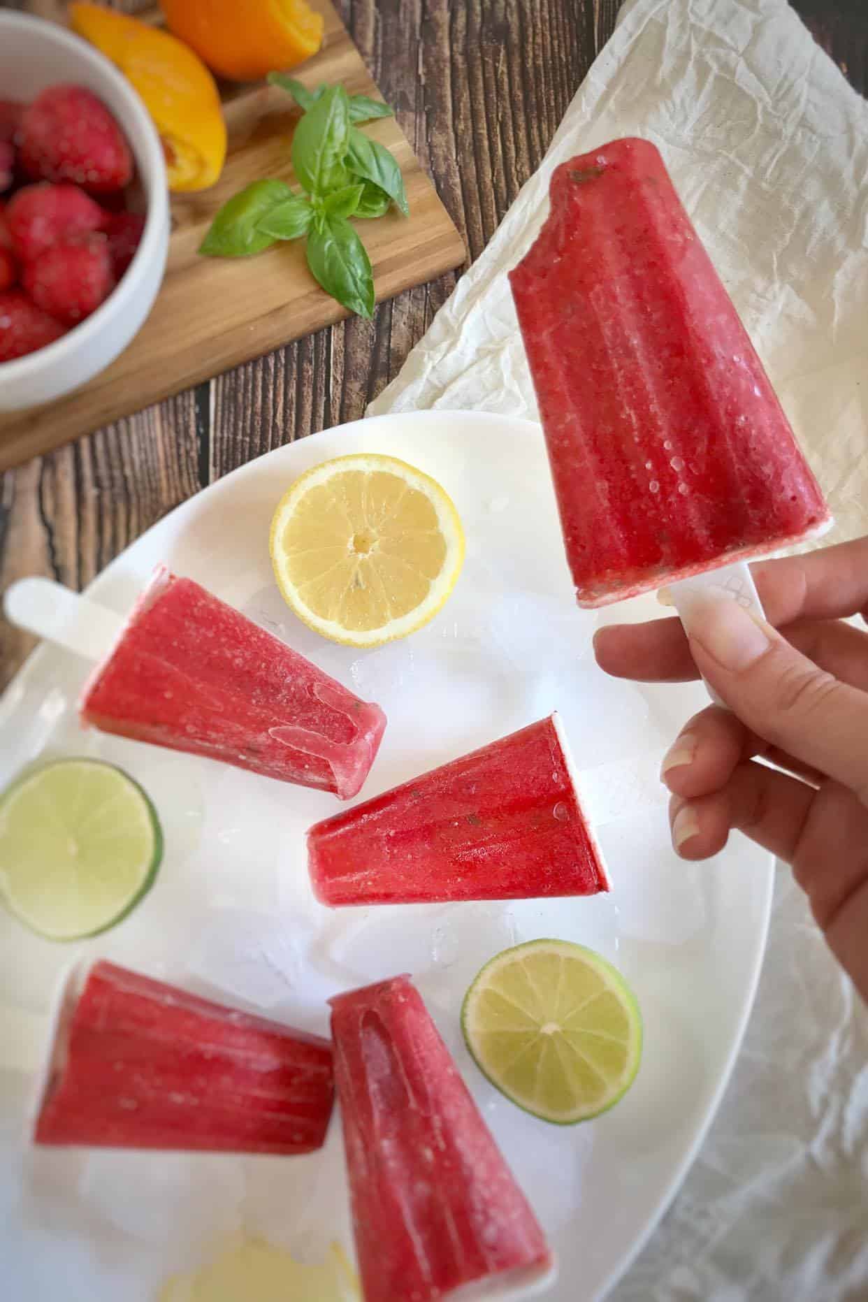 Hand holding a strawberry popsicle above a plate with more popsicles.
