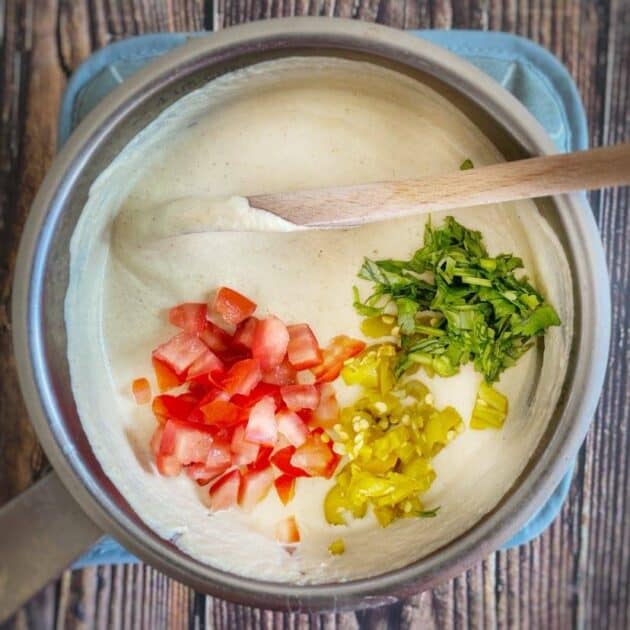 Cashew queso in a pot with tomatoes, chilis, and cilantro.