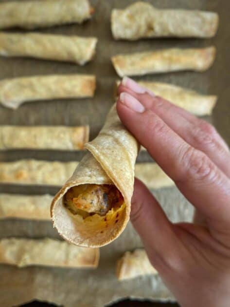 Hand picking up a baked vegan taquito.