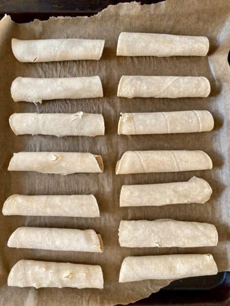 Rolled taquitos on a baking sheet.