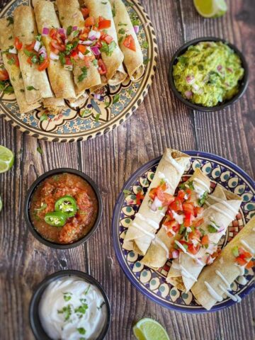 Vegan taquitos on two plates with small bowls of salsa and guacamole.