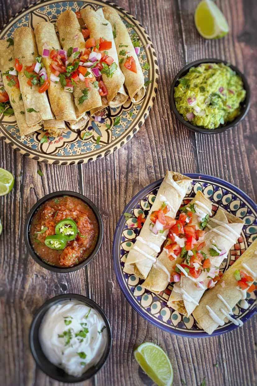 Vegan taquitos on two plates with small bowls of salsa and guacamole.