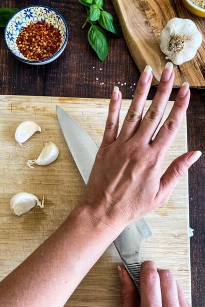 Hand using a knife to flatten garlic.