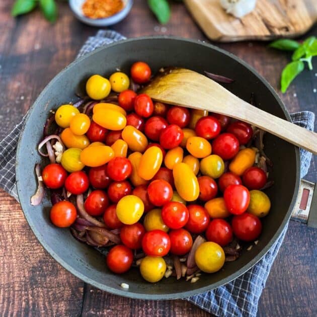 Cherry tomatoes added to a skillet with cooked onion.