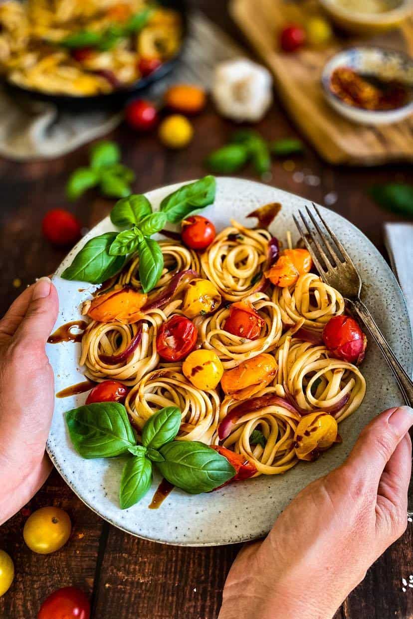 Hands holding a bowl of cherry tomato pasta.