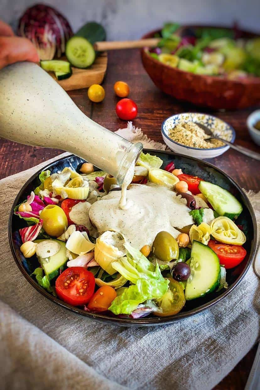 Jar of creamy Italian dressing being poured onto a salad.