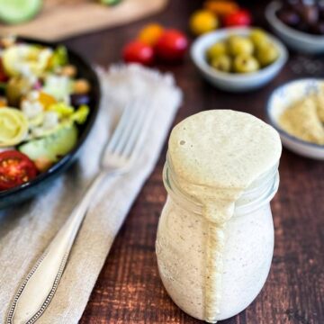 Jar of vegan Italian dressing next to a bowl of salad.