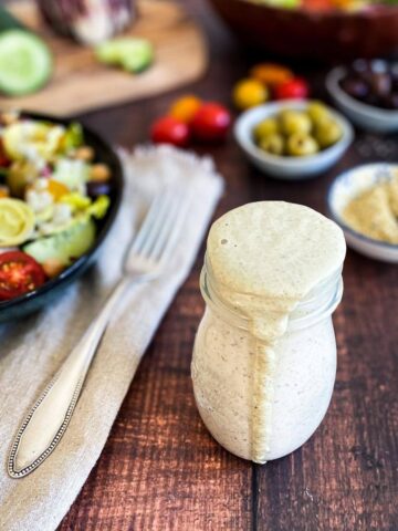 Jar of vegan Italian dressing next to a bowl of salad.