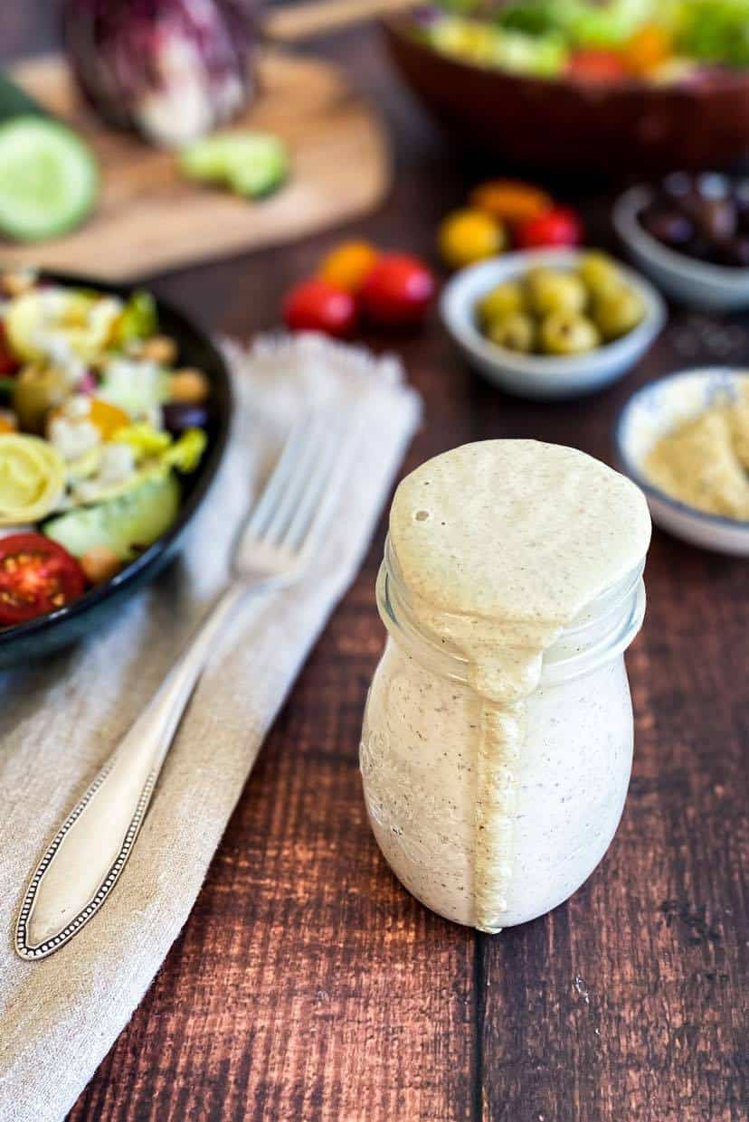 Jar of vegan Italian dressing next to a bowl of salad.