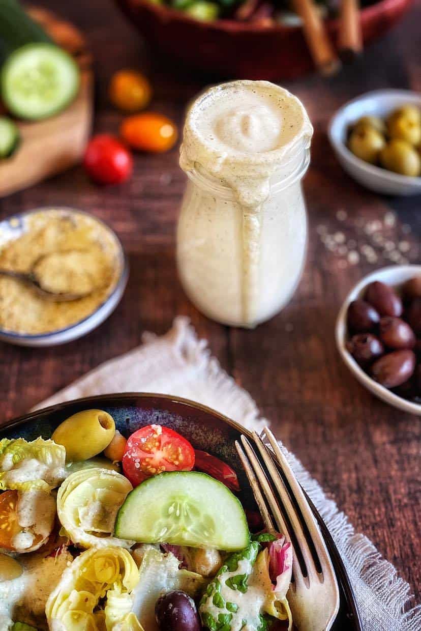 Vegan Italian dressing in a jar surrounded by salad and other igredients.