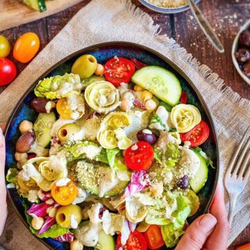 Hands holding a bowl of vegan Italian salad.