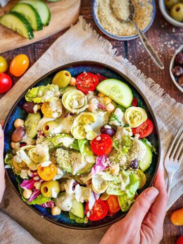 Hands holding a bowl of vegan Italian salad.