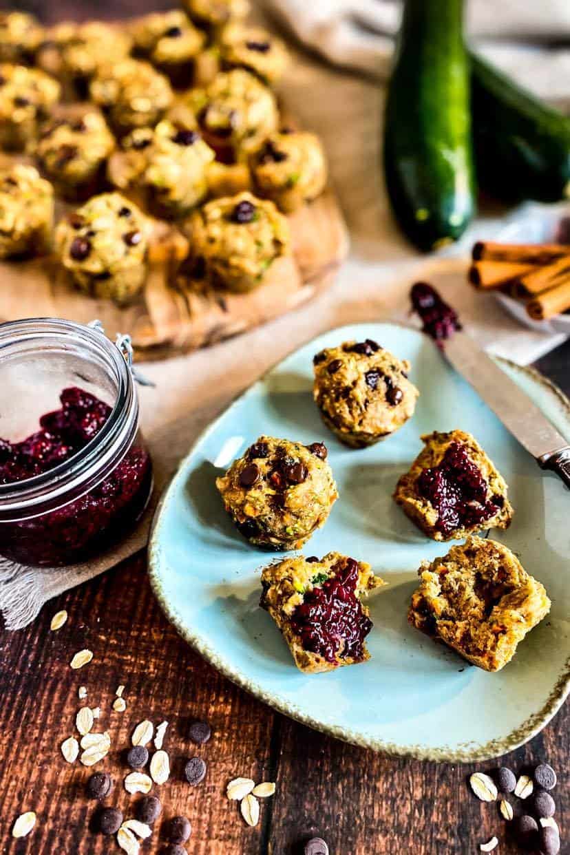 Plate with vegan zucchini muffins. Some are cut with jam on top.