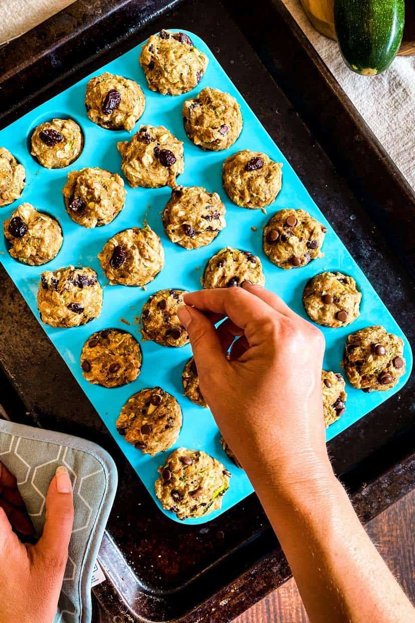 Hand testing vegan zucchini muffins with a tothpick.