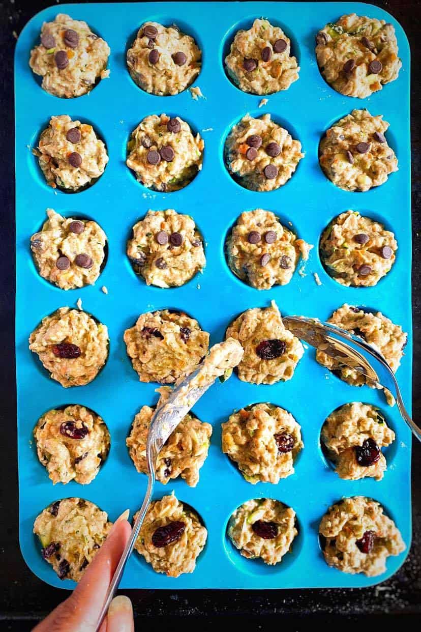 Spoons adding muffin batter to a silicone form.