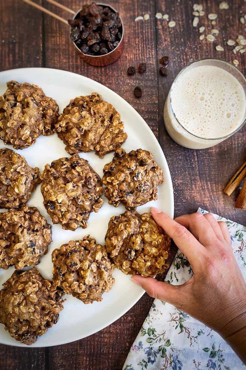 Platter with vegan oatmeal raisin cookies, side of oat milk and raisins in measuring cup.