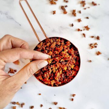 Hand picking up vegan bacon bits from a measuring cup.