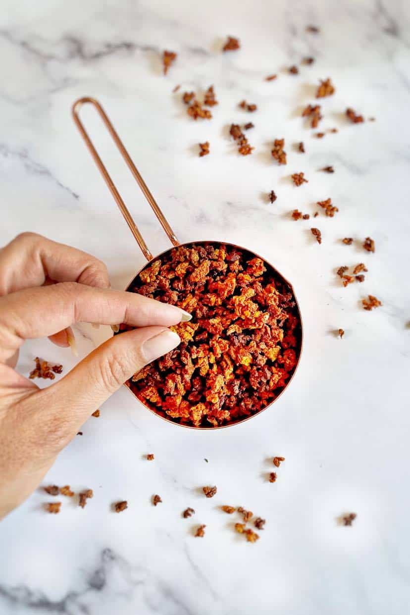 Hand picking up vegan bacon bits from a measuring cup.