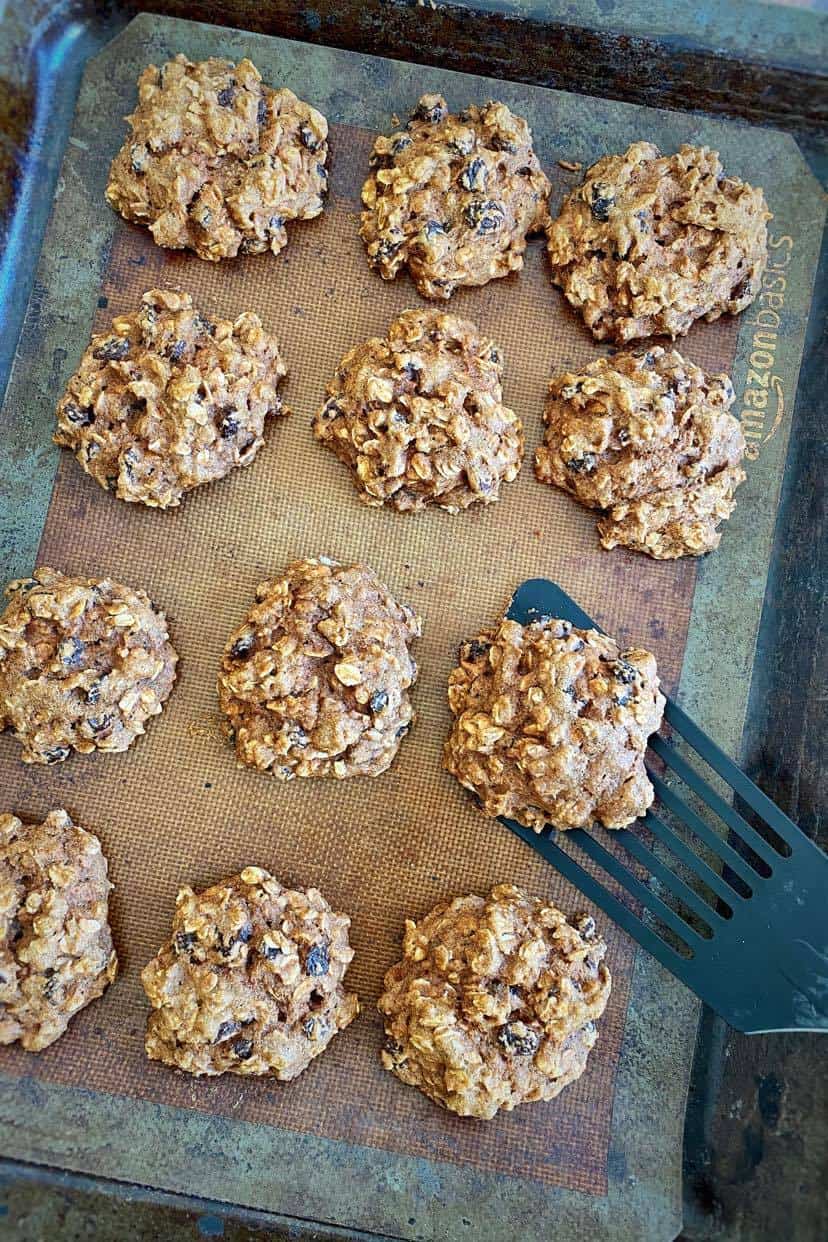 Vegan oatmeal raisin cookies baked on a cookie sheet with a spatula lifting one up.