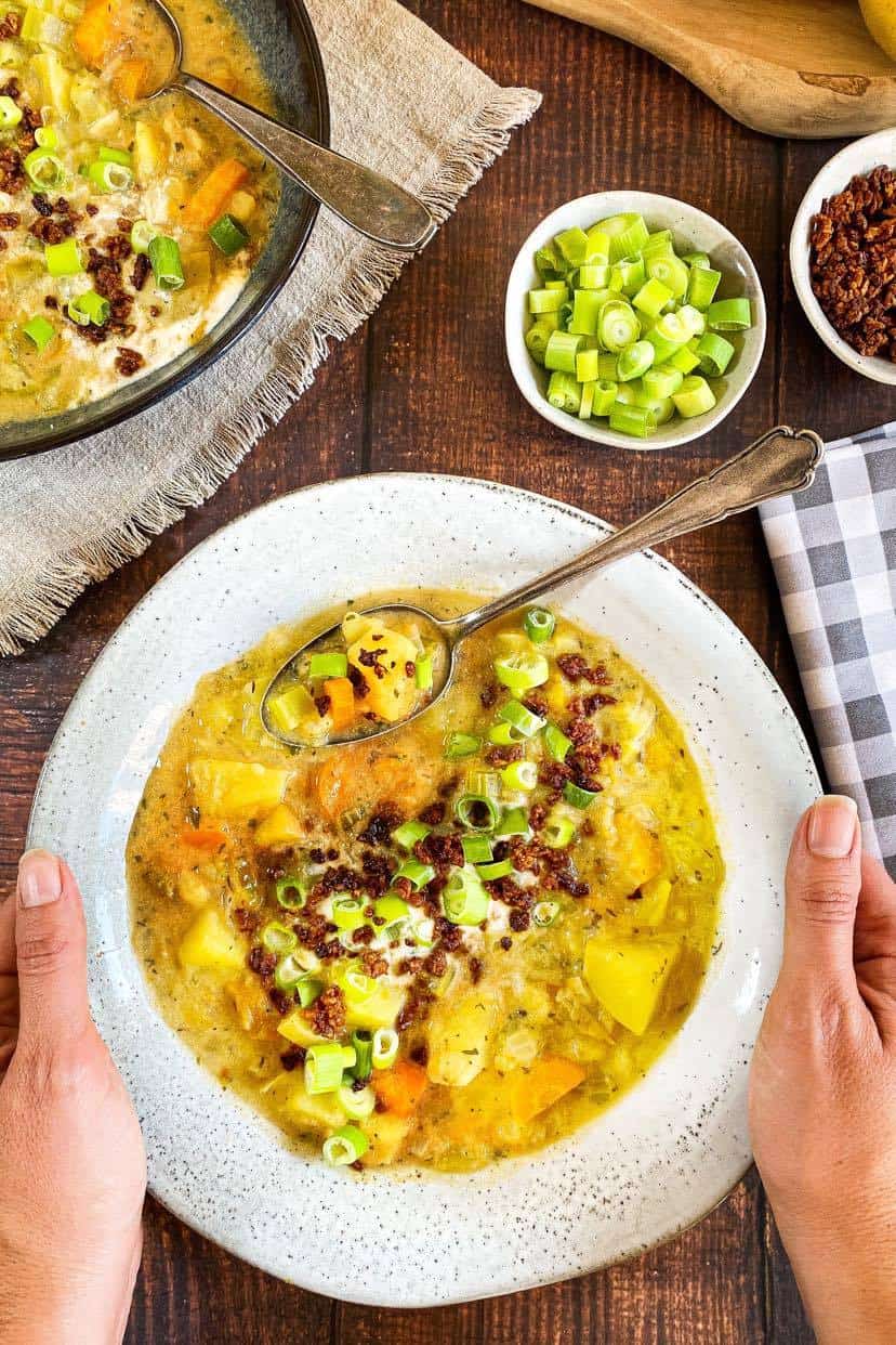 Two hands holding bowl of potato soup with spoon.