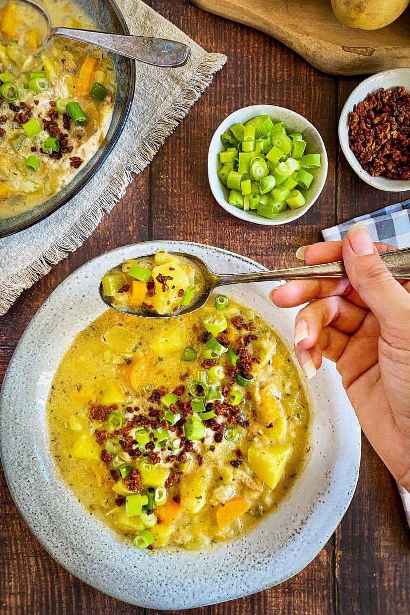 Bowl of potato soup with hand holding spoon.
