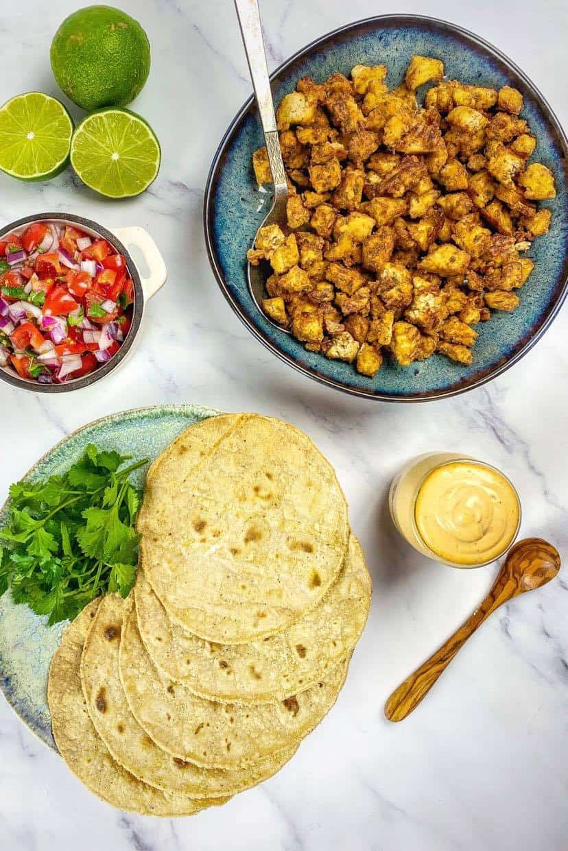 Tofu in a bowl next to taco shells and pico de gallo.