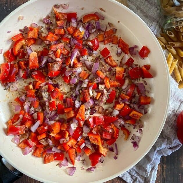 Red onions and bell peppers cooking in a skillet.