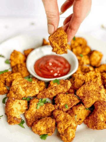 Hand dipping air fryer tofu nugget into ketchup.