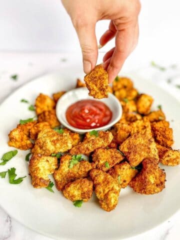 Hand dipping air fryer tofu nugget into ketchup.