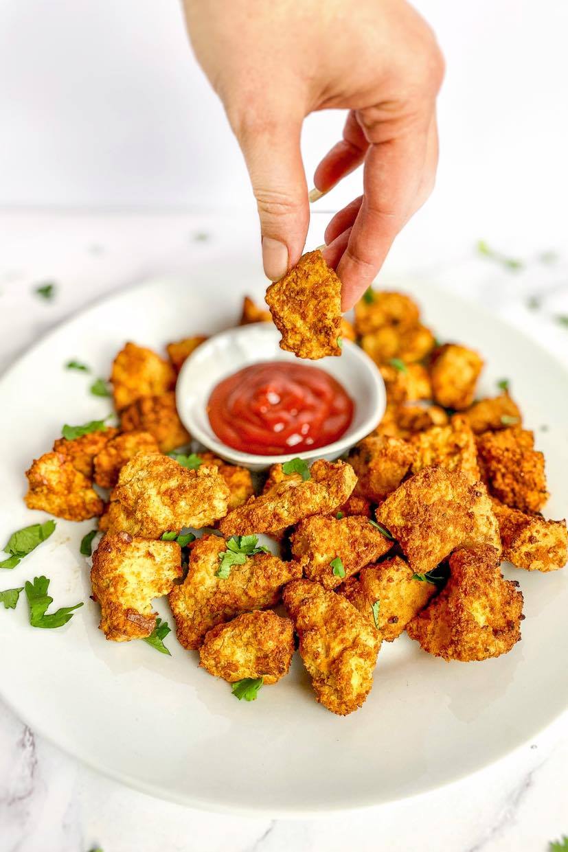 Hand dipping air fryer tofu nugget into ketchup.