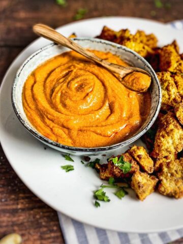 Vegan buffalo sauce in a bowl surrounded by tofu nuggets.