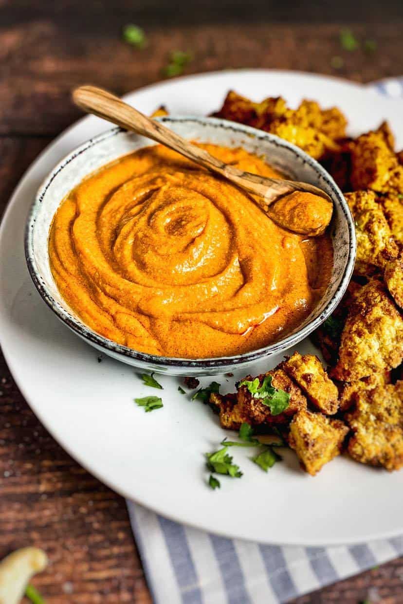 Vegan buffalo sauce in a bowl surrounded by tofu nuggets.