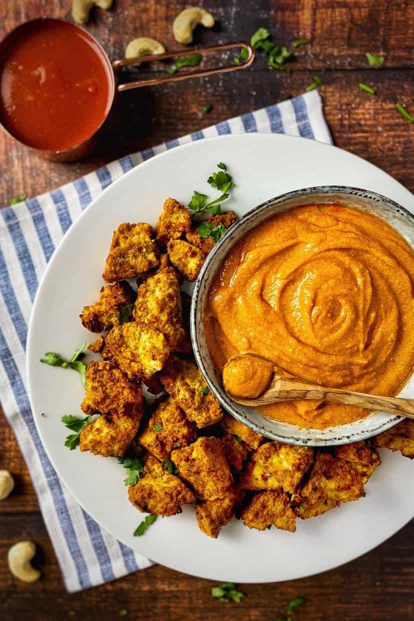 Vegan buffalo sauce in a bowl surrounded by tofu nuggets.