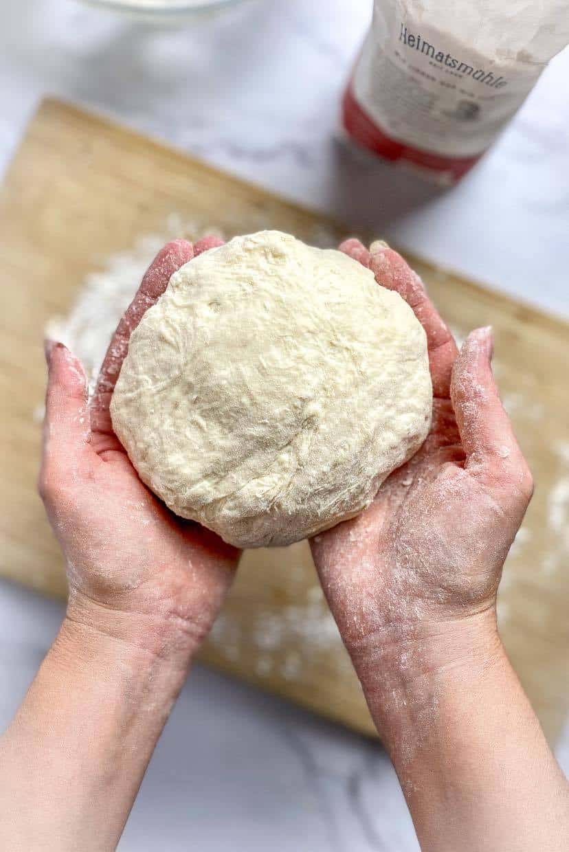 Hands holding a ball of pizza dough.