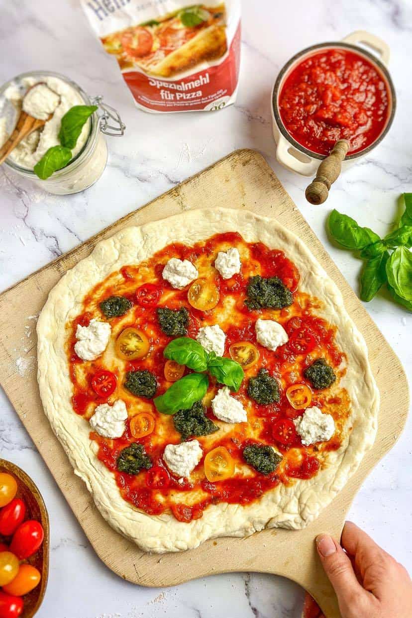 Uncooked vegan pesto pizza on a wooden paddle.