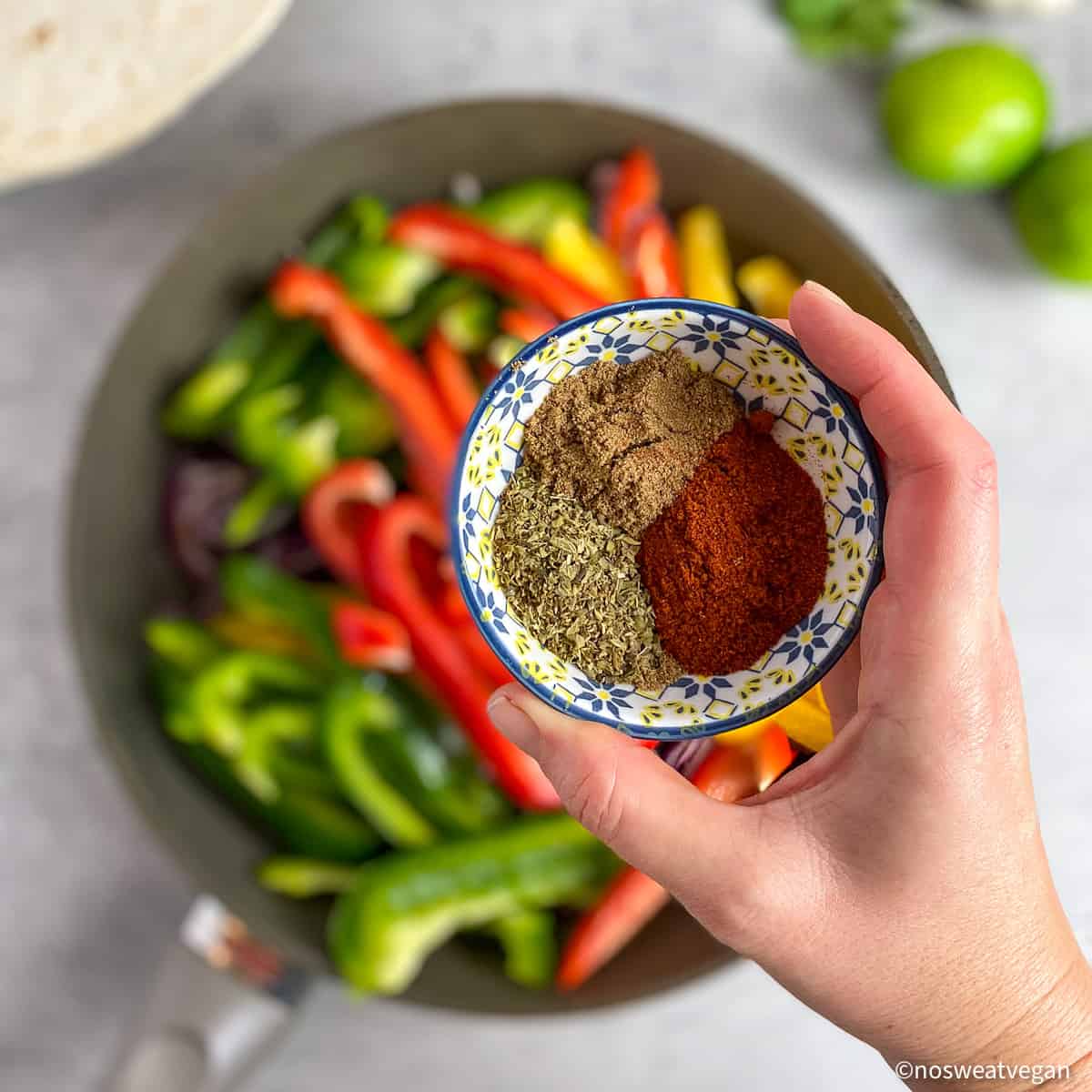 Hand holding seasoning over a skillet of fajitas.