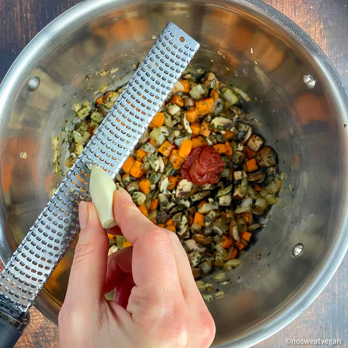 Pot with vegetables and tomato paste. Hand grating garlic with a Microplane.