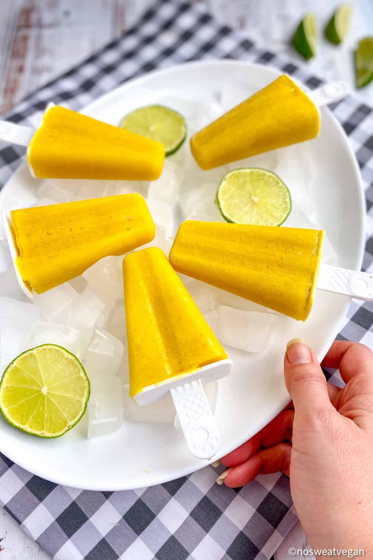 Vegan mango lassi popsicles on a plate with limes.