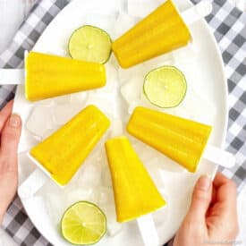 Mango popsicles on a plate with ice and limes.