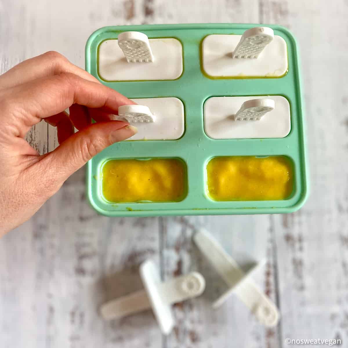 Mango popsicles in forms with lids going on.