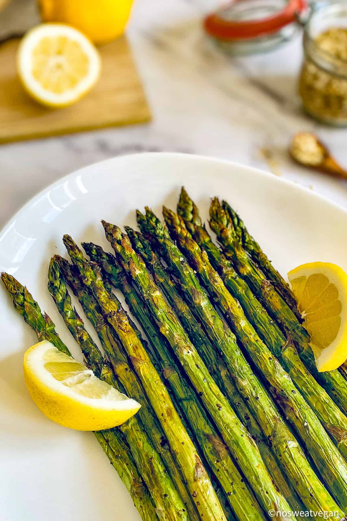 Air fried asparagus on a plate with lemon wedges.