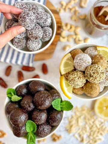 Vegan bliss balls in three bowls with a hand picking up one.